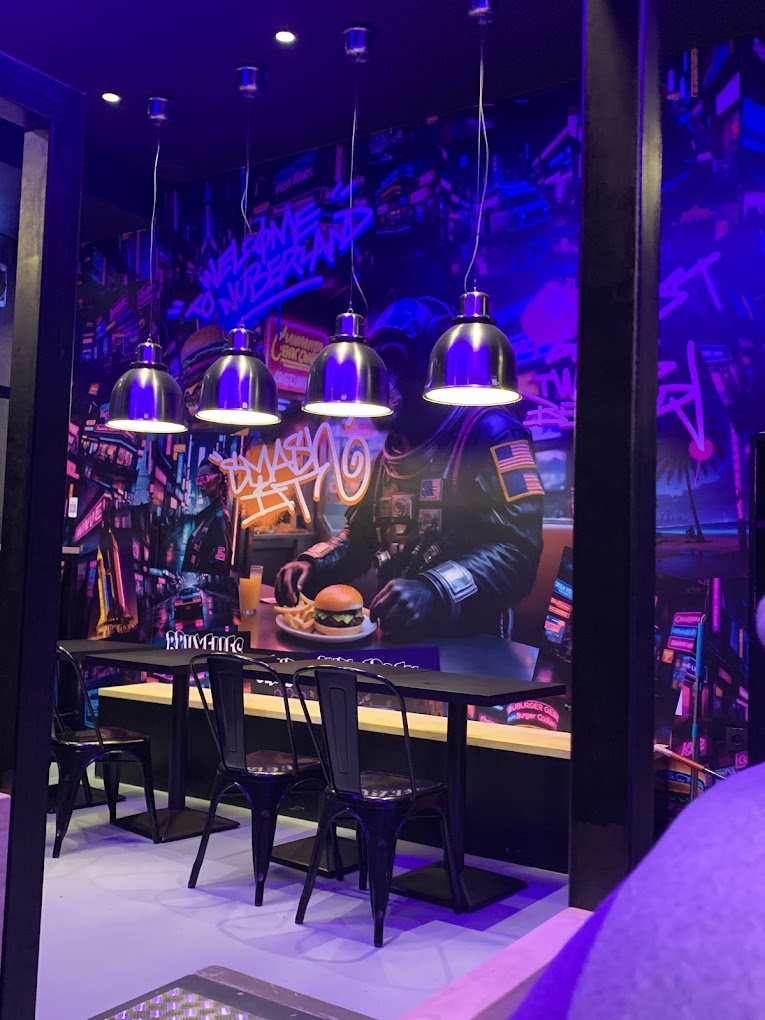 The interior of halal restaurant Nub Smashburger in Antwerpen, Belgium, showing a vibrant mural featuring a figure in a space suit, modern lighting, and black chairs around a long table.