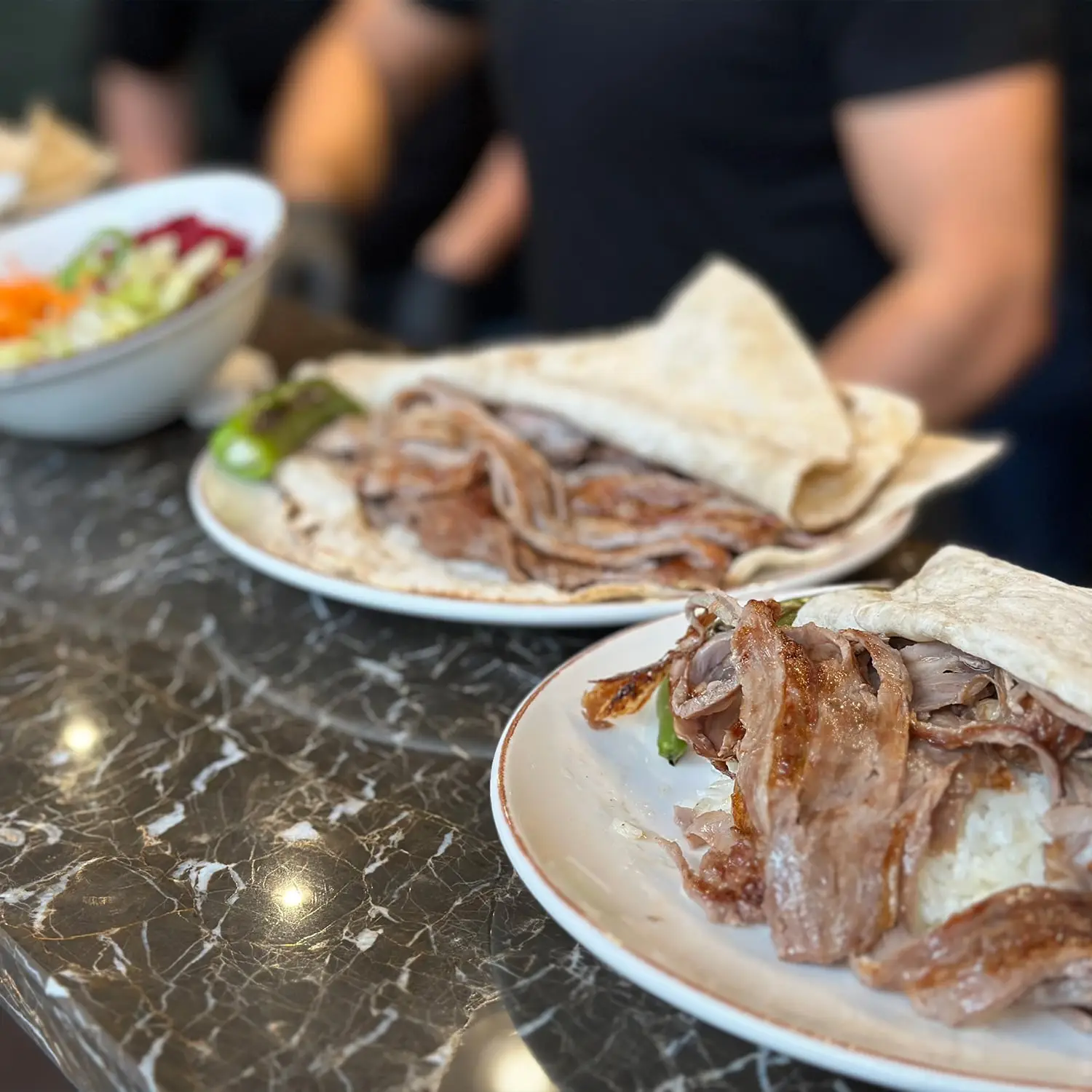 A plate of thinly sliced meat wrapped in flatbread, served with rice and a side of salad at Harbii, a halal restaurant in Rotterdam, Netherlands.
