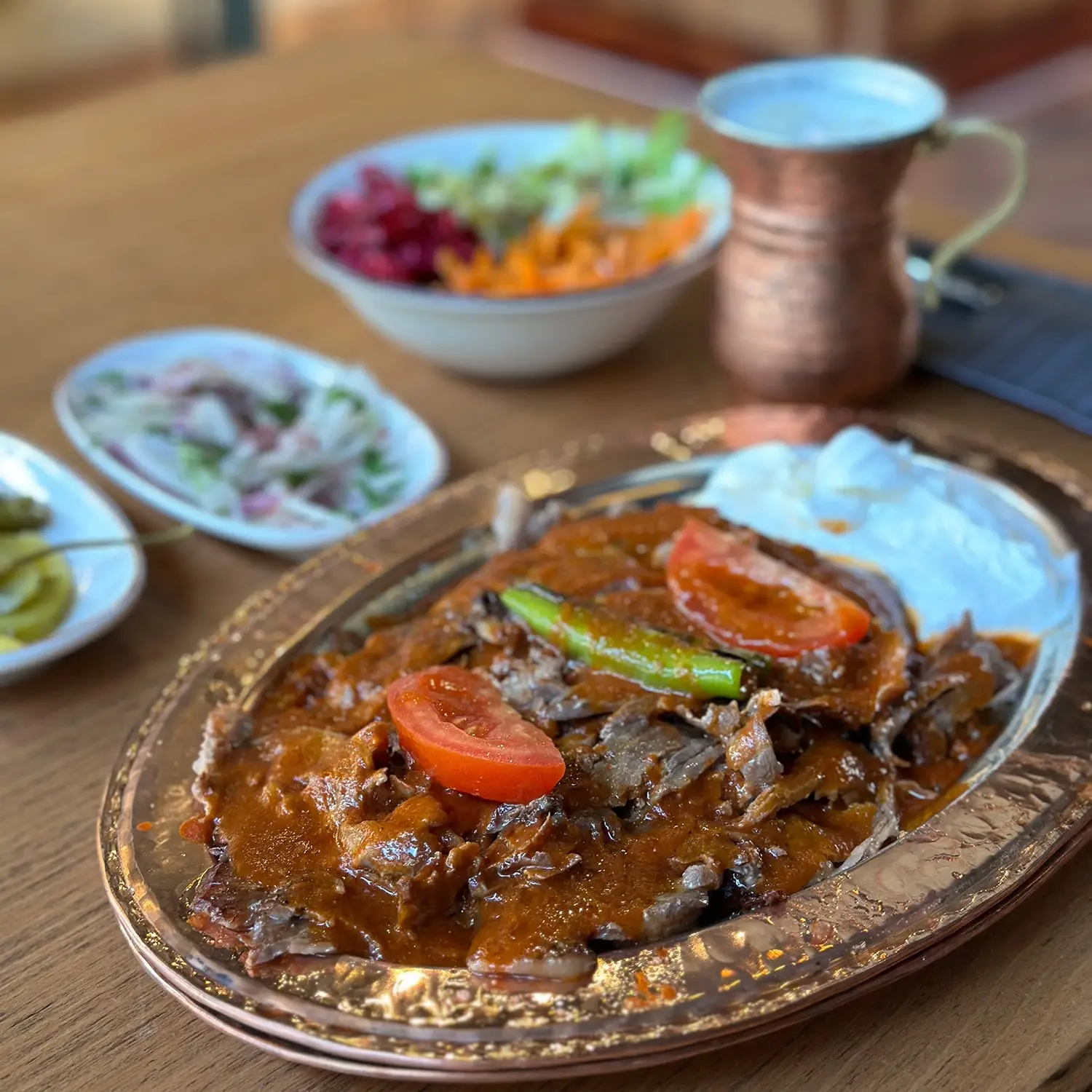 A plate of tender meat in a rich sauce, garnished with tomatoes and green pepper, served with yogurt at Harbii, a halal restaurant in Rotterdam, Netherlands.