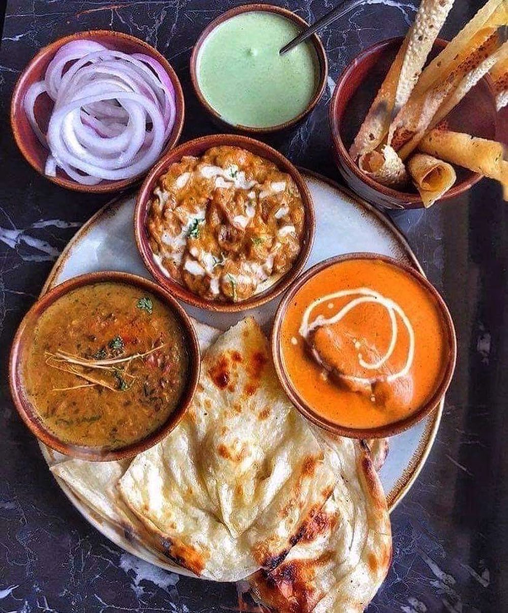 Een bord met naanbrood, dal en twee soorten curry, vergezeld van gesneden uien en groene saus bij Curryosity, een halal restaurant in Antwerpen, België.