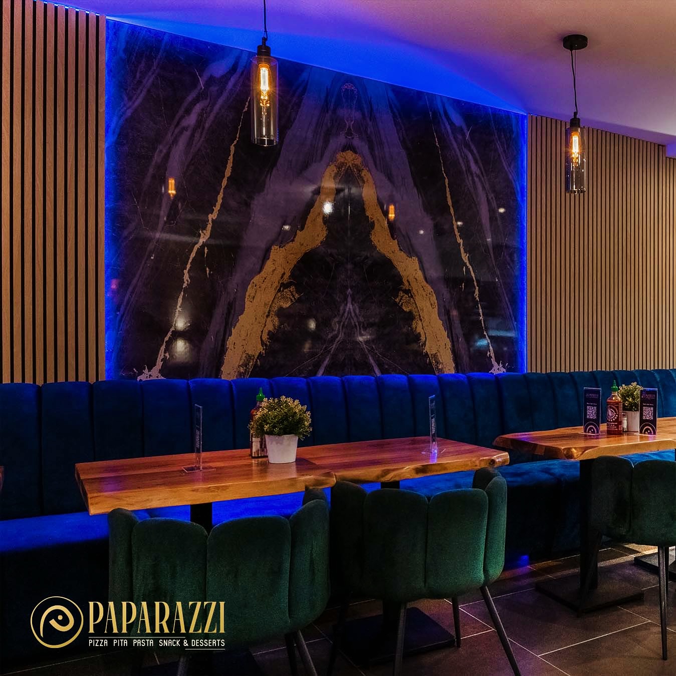 The interior of halal restaurant Paparazzi Bistro in Antwerpen, Belgium, showing blue lighting, a marble wall, wooden tables, and green upholstered seating.