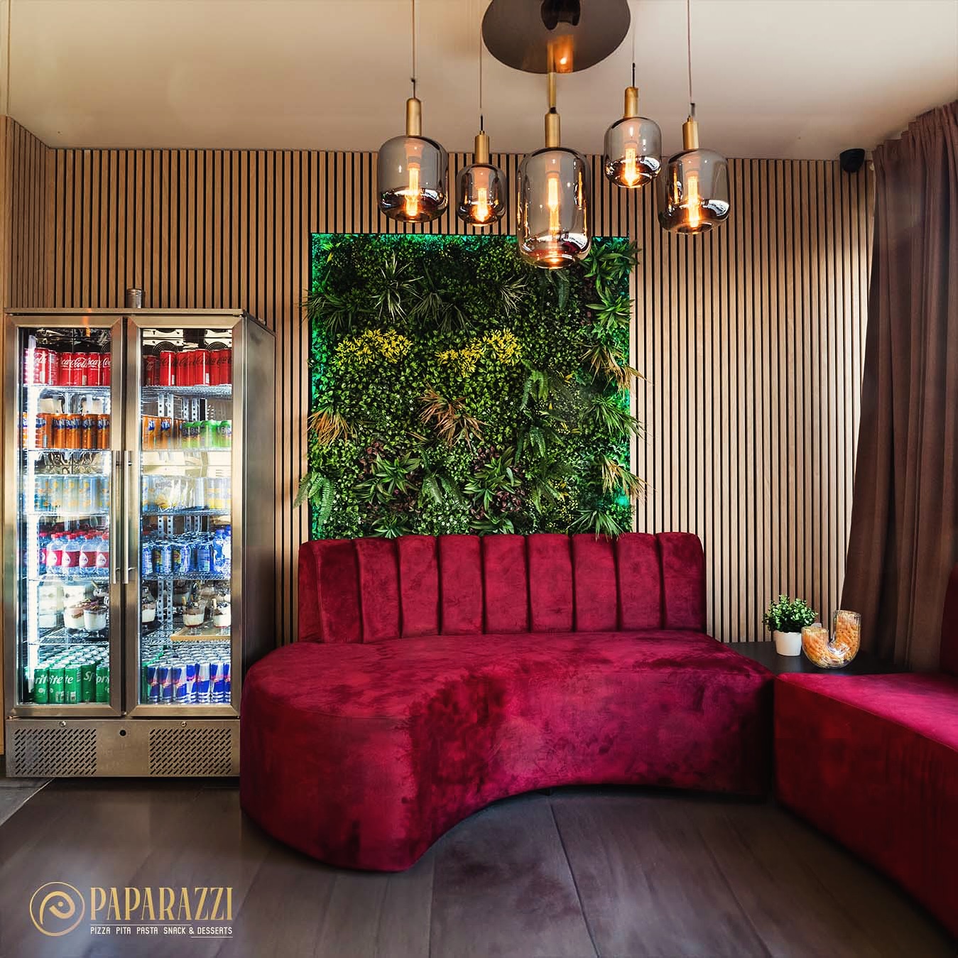 The interior of halal restaurant Paparazzi Bistro in Antwerpen, Belgium, showing a red velvet curved seating area, a green vertical garden, and a glass refrigerator filled with beverages.