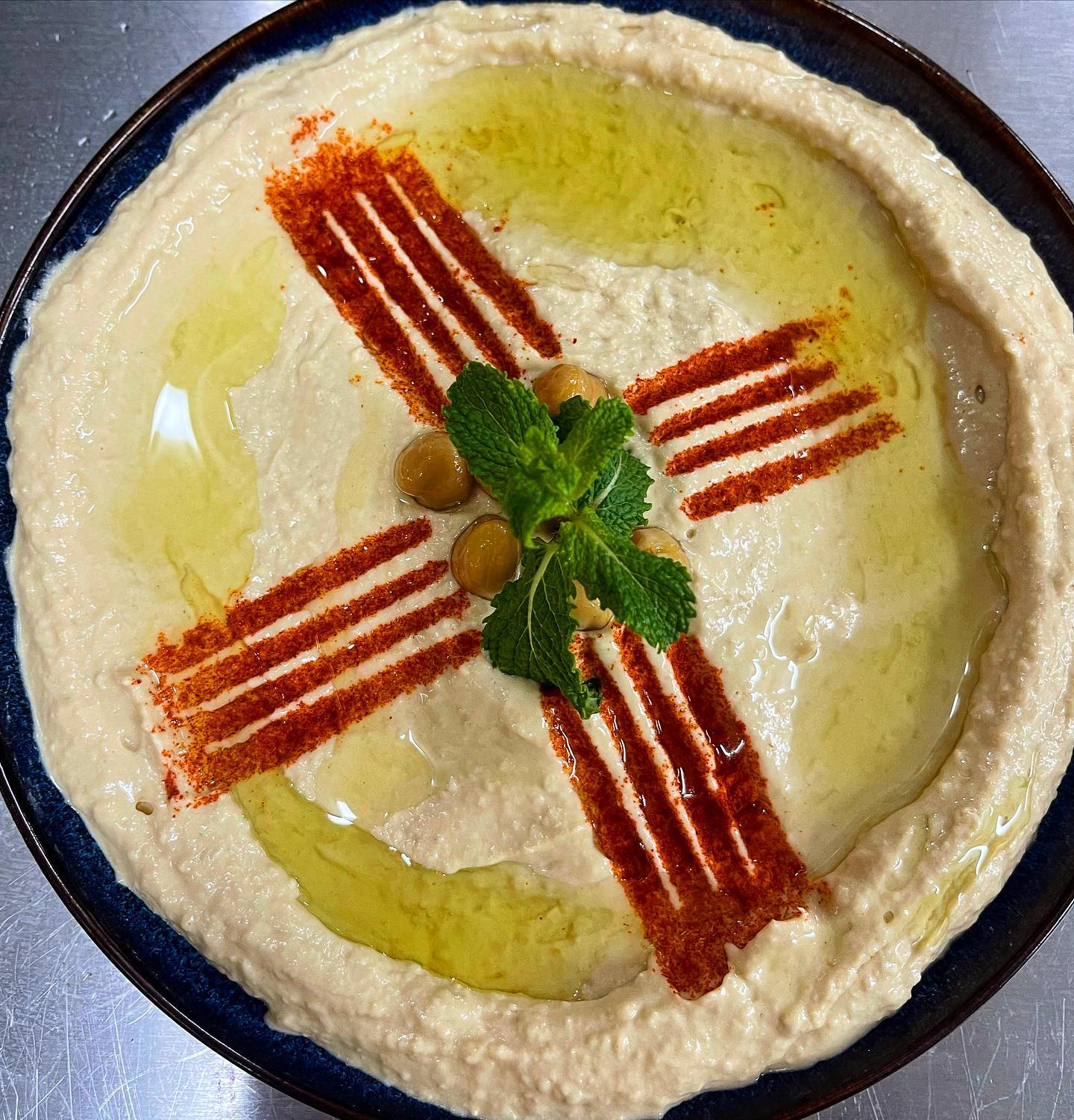 A plate of hummus garnished with olive oil, paprika, and mint leaves at Liva Restaurant & Café, a halal restaurant in Antwerpen, Belgium.