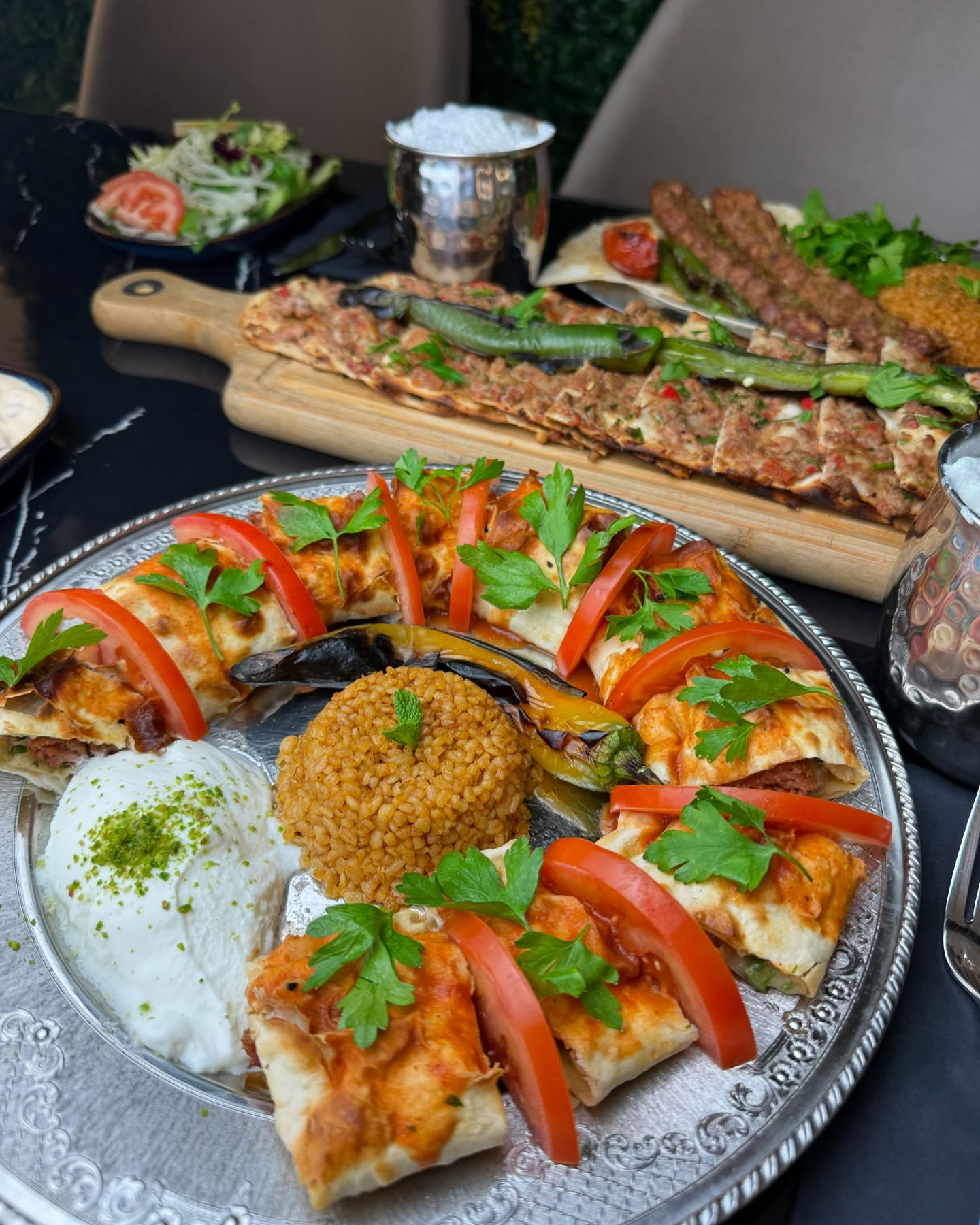 A platter of baked flatbreads topped with minced meat, tomatoes, and parsley, served with yogurt, bulgur, and grilled vegetables at Liva Restaurant & Café, a halal restaurant in Antwerpen, Belgium.