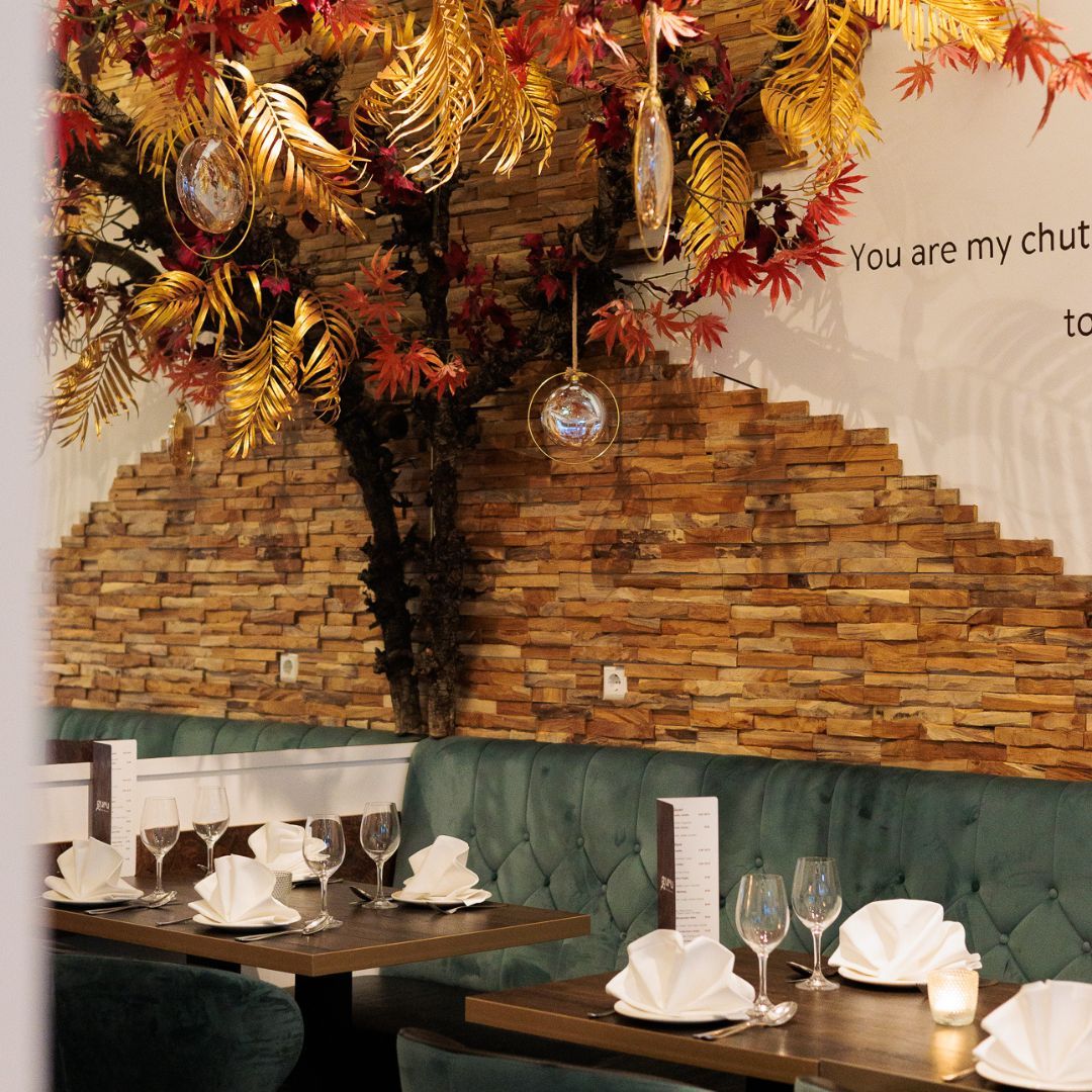 The interior of halal restaurant Guru in Amsterdam, Netherlands, showing green velvet seating, wooden wall decor, and decorative hanging plants.