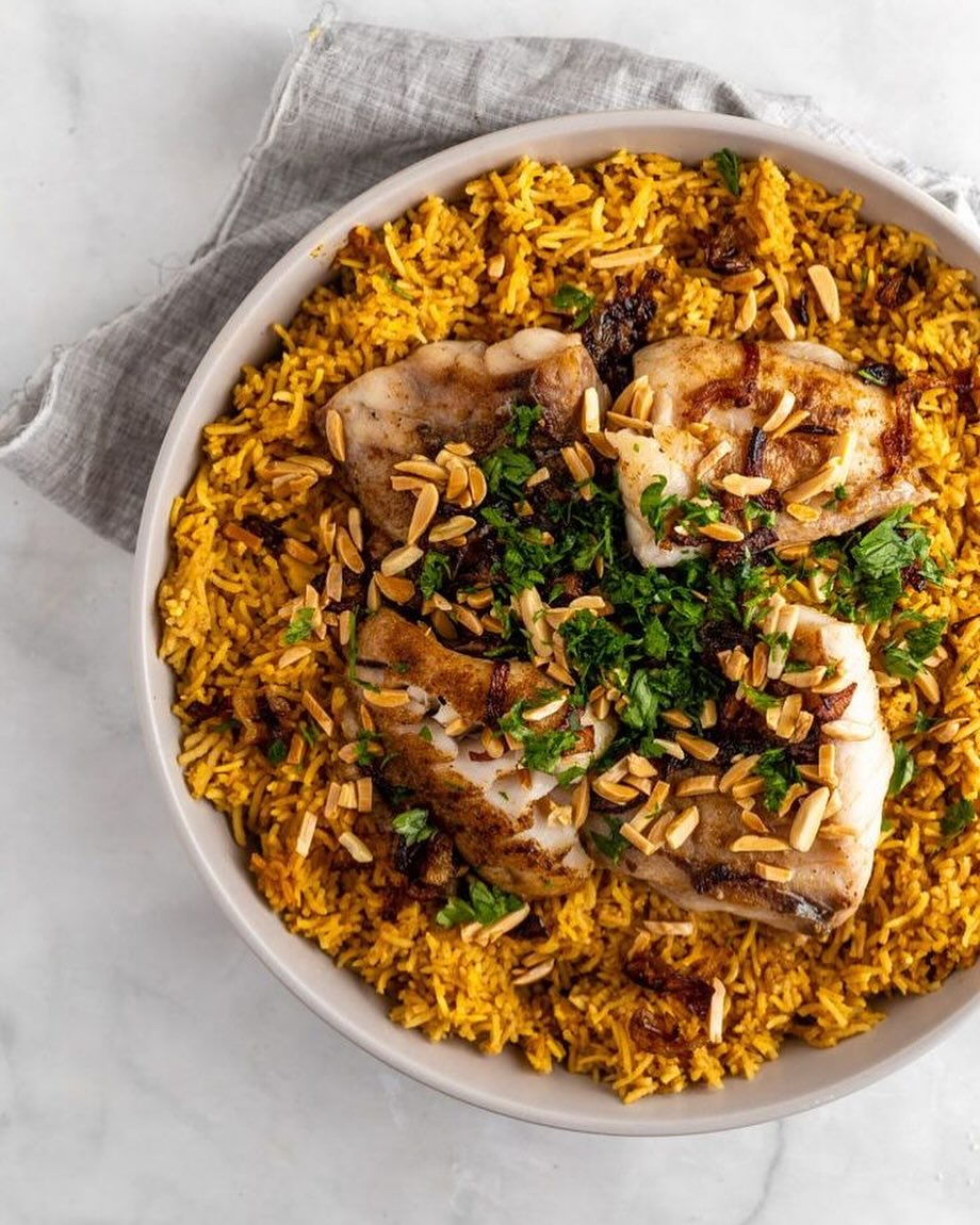 A plate of spiced rice topped with grilled fish, garnished with chopped herbs and toasted almonds at Olive, a halal restaurant in Saint-Gilles, Belgium.