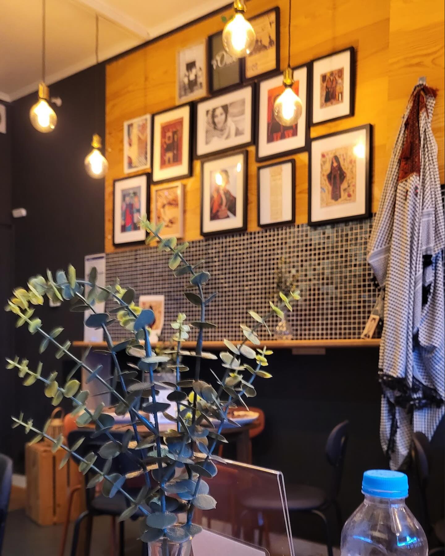 The interior of halal restaurant Olive in Saint-Gilles, Belgium, showing framed pictures on the wall, hanging light bulbs, a wooden panel, and a small plant on the table.