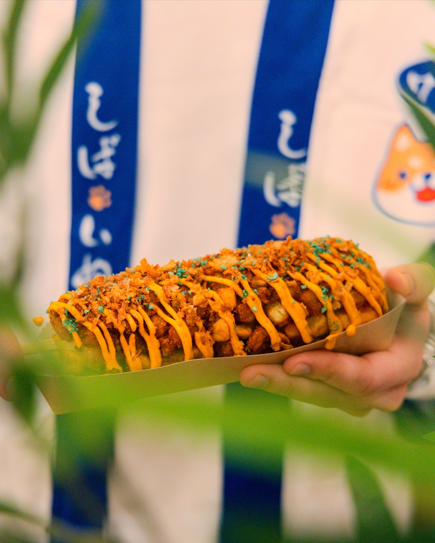 A corndog topped with orange sauce and crunchy toppings at Sekaï Corndogs, a halal restaurant in Bruxelles, Belgium.