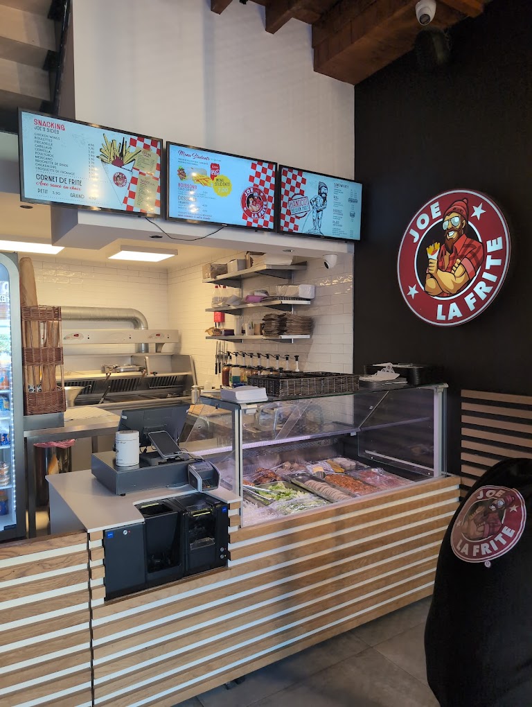 The interior of halal restaurant Joe La Frite in Bruxelles, Belgium, showing a counter with a cash register, display cases with food items, and digital menu screens.