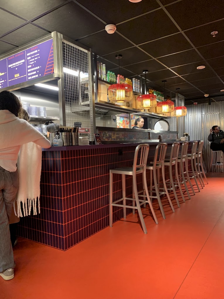 Het interieur van halal restaurant Seoul South Station in Brussel, België, met een bar met hoge stoelen, kleurrijke hangende lantaarns en een menubord.