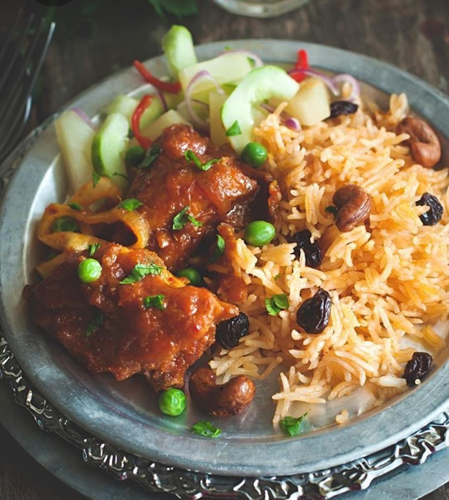 A plate of chicken in a rich sauce served with spiced rice, green peas, and a side salad at Leuven Chicken and Rice, a halal restaurant in Leuven, Belgium.