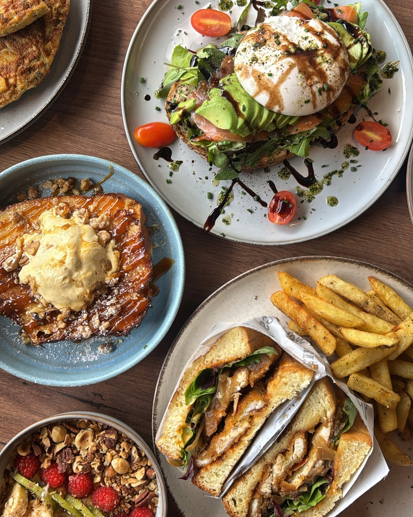 A plate of various dishes including a sandwich with fried chicken, salad, and fries, a dessert with caramel and ice cream, and a bowl of granola with berries at Baba Brunch, a halal restaurant in Koekelberg, Belgium.