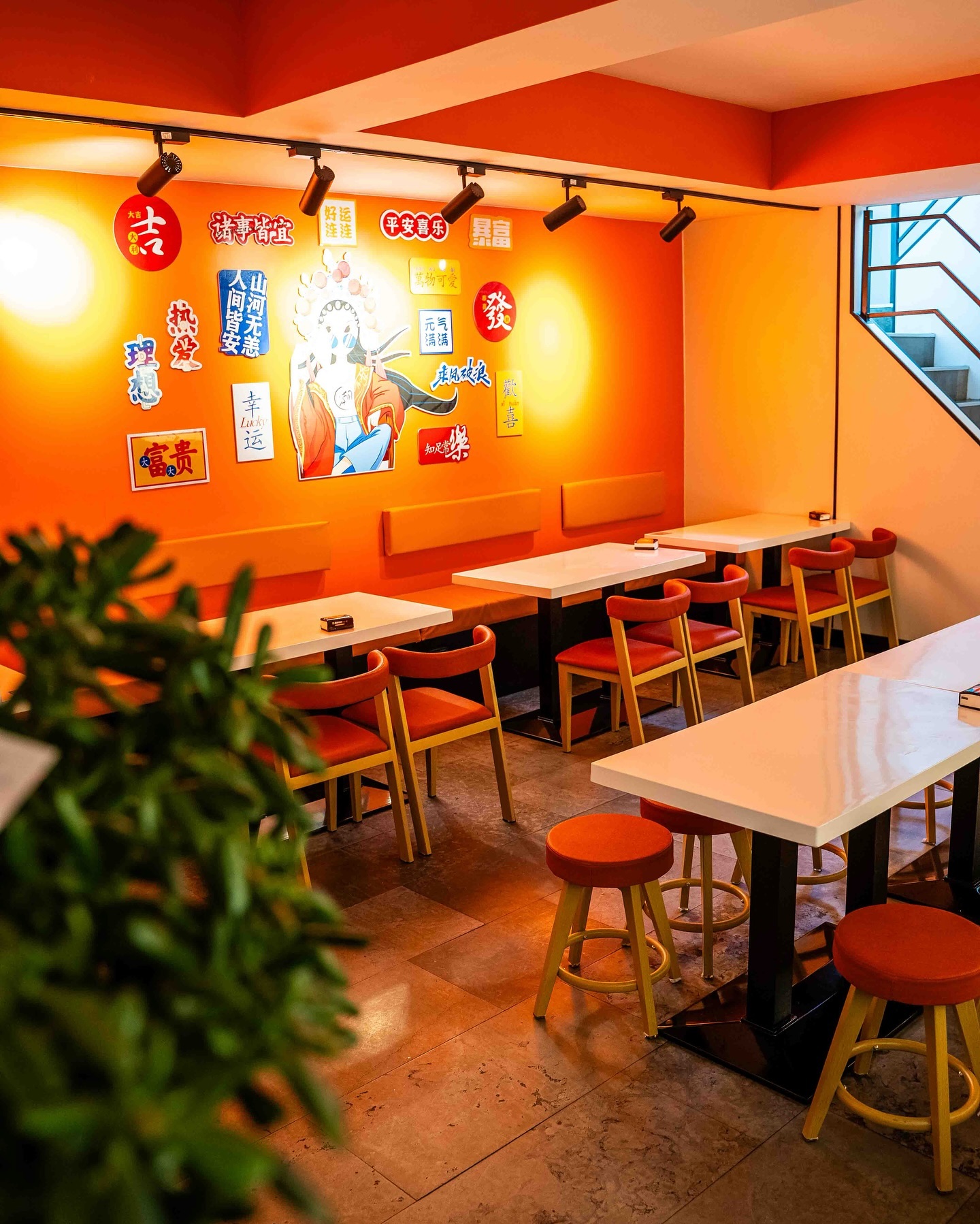 The interior of halal restaurant ZLMLT in Rotterdam, Netherlands, showing orange walls adorned with various colorful signs and a seating area with white tables and red chairs.