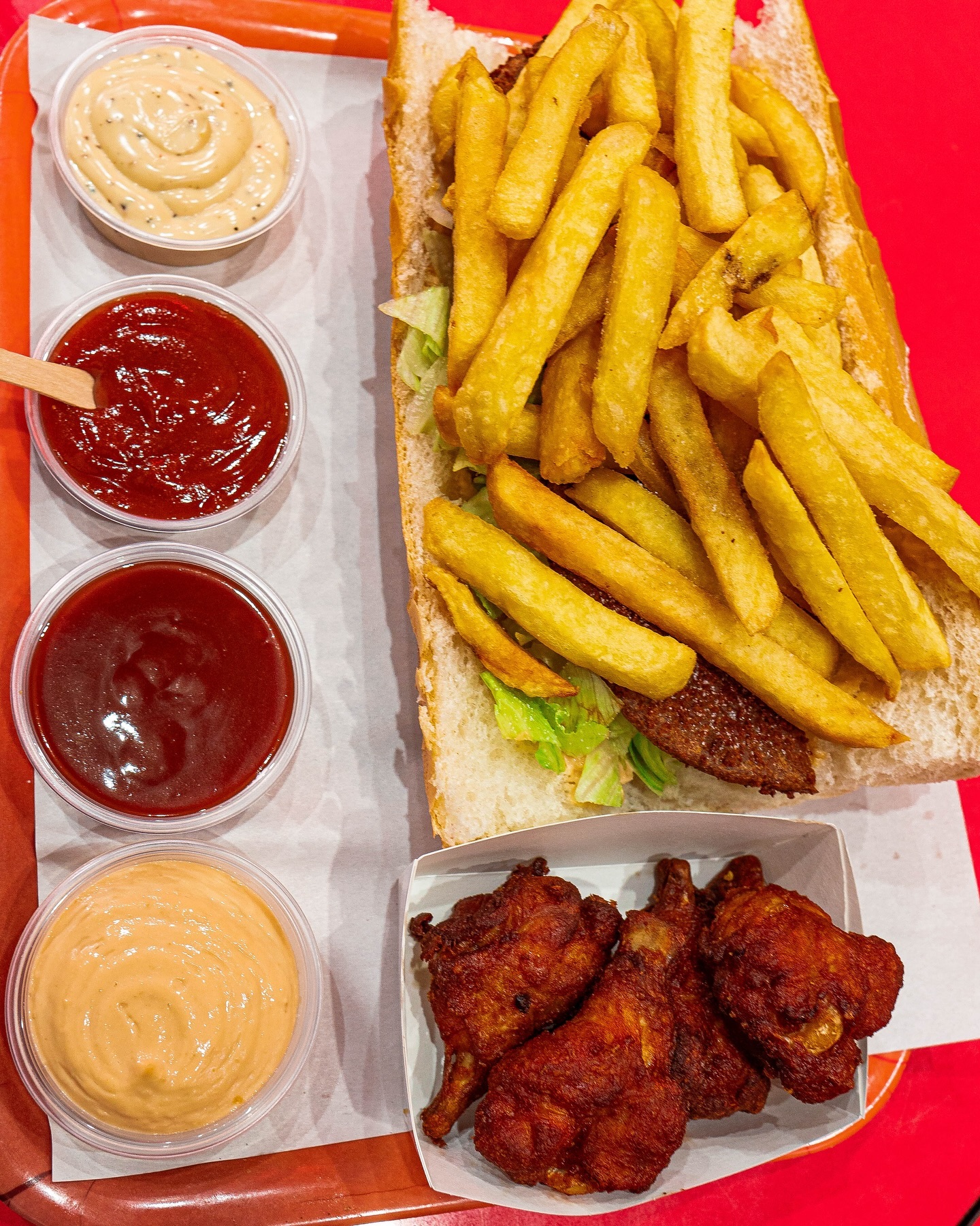 Een bord frietjes met sla en een gefrituurde vleespastei, vergezeld van kippenvleugels en verschillende sauzen bij Batata, een halal restaurant in Anderlecht, België.
