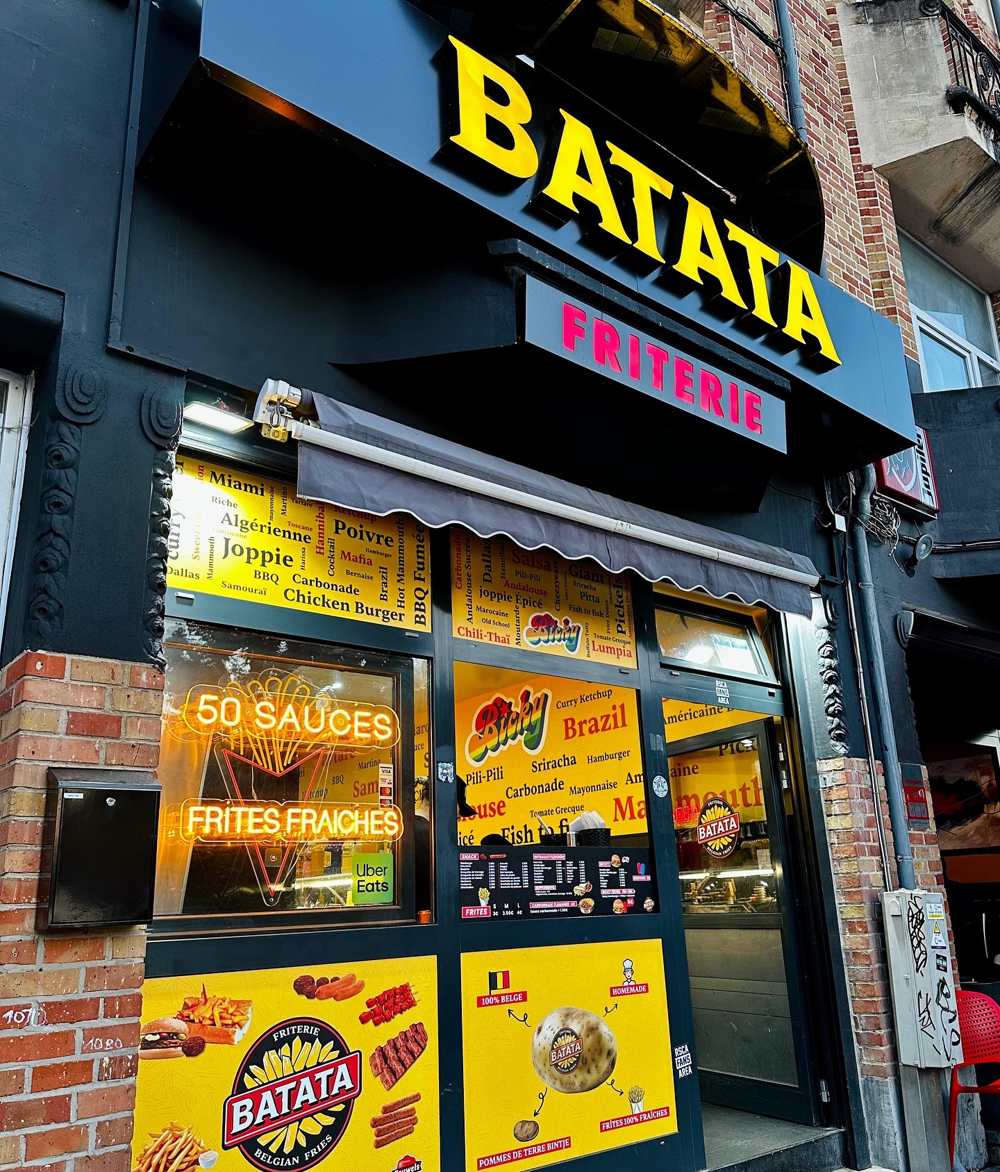 De buitenkant van halal restaurant Batata in Anderlecht, België, met een heldere sign met de naam 'BATATA' en 'FRITERIE', samen met een menu met verschillende sauzen en gerechten.