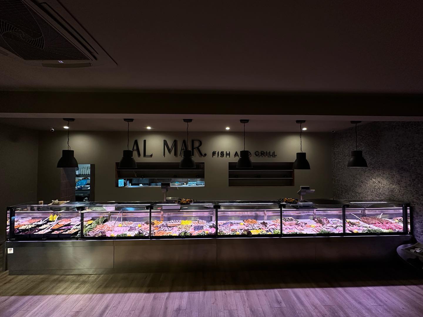 The interior of halal restaurant Al Mar in Antwerpen, Belgium, showing a display case filled with various seafood and meats under bright lighting.