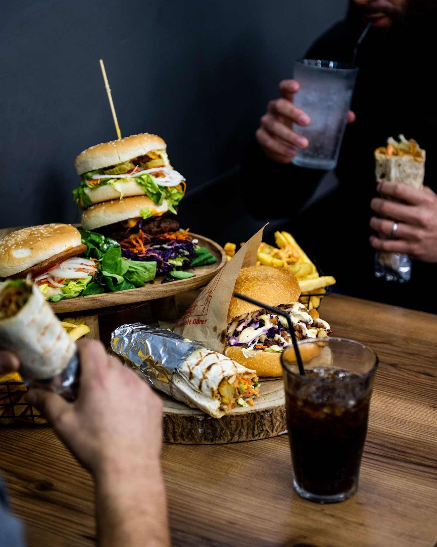Un burger empilé avec de la laitue, des tomates et des cornichons, accompagné de frites et d'un wrap au Snack Murat, un restaurant halal à Saint-Gilles, Belgique.