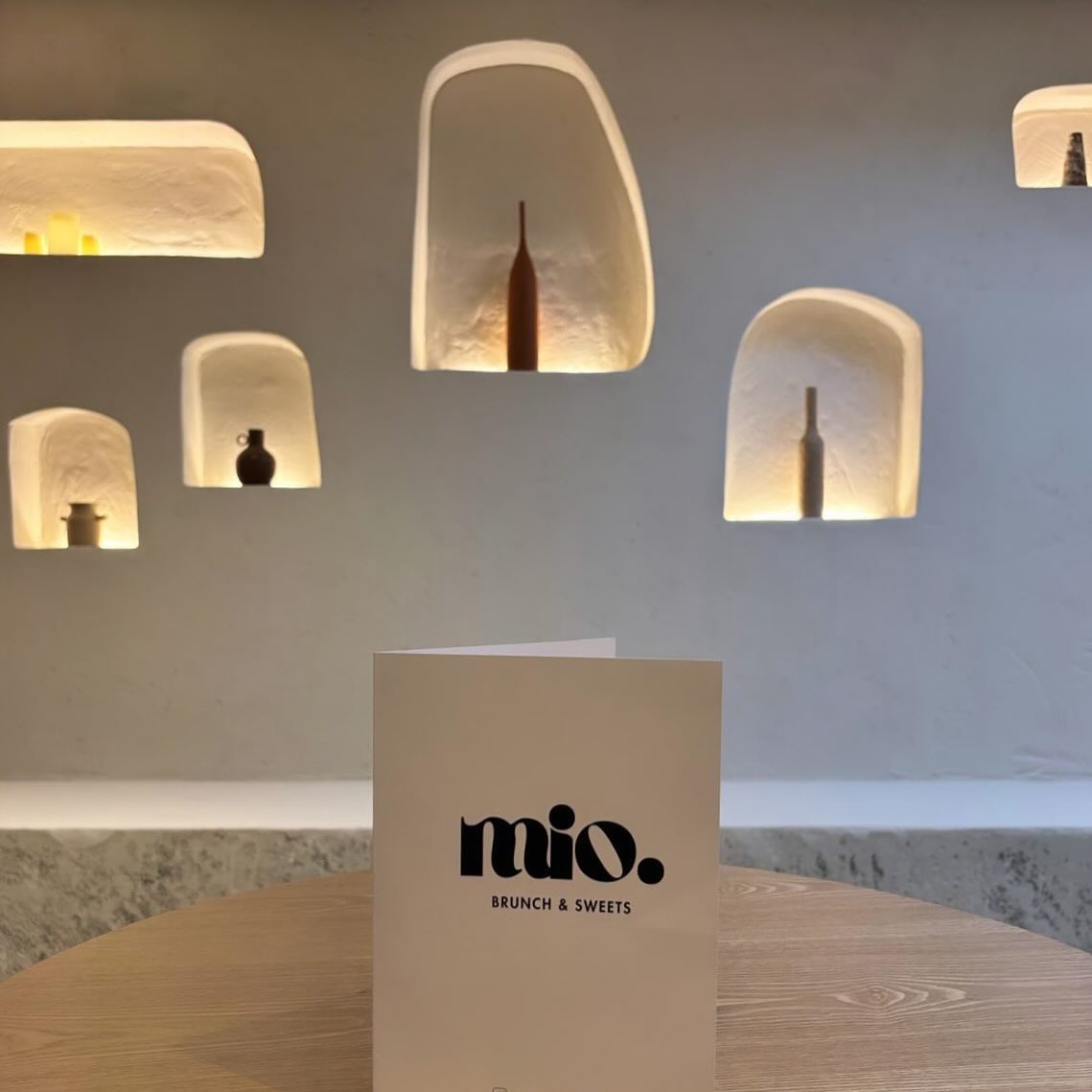 L'intérieur du restaurant halal Mio à Anvers, en Belgique, montrant un design minimaliste avec des niches illuminées affichant des objets décoratifs et un menu sur une table en bois.